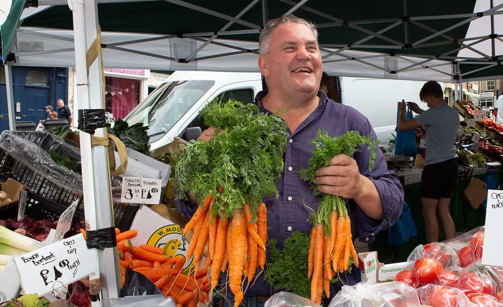 Image of market trader on fruit and vegetable stall, surrounded by local produce