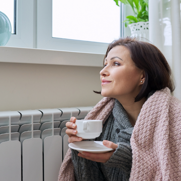 Image shows a woman getting warm by a radiator